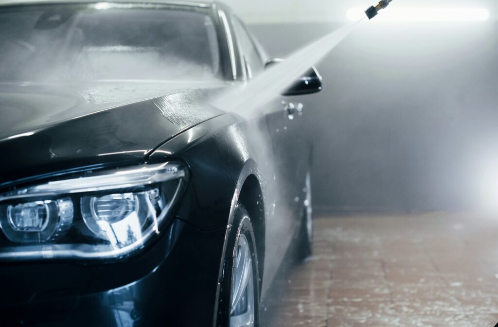 High pressured water. Modern black automobile get cleaned inside of car wash station