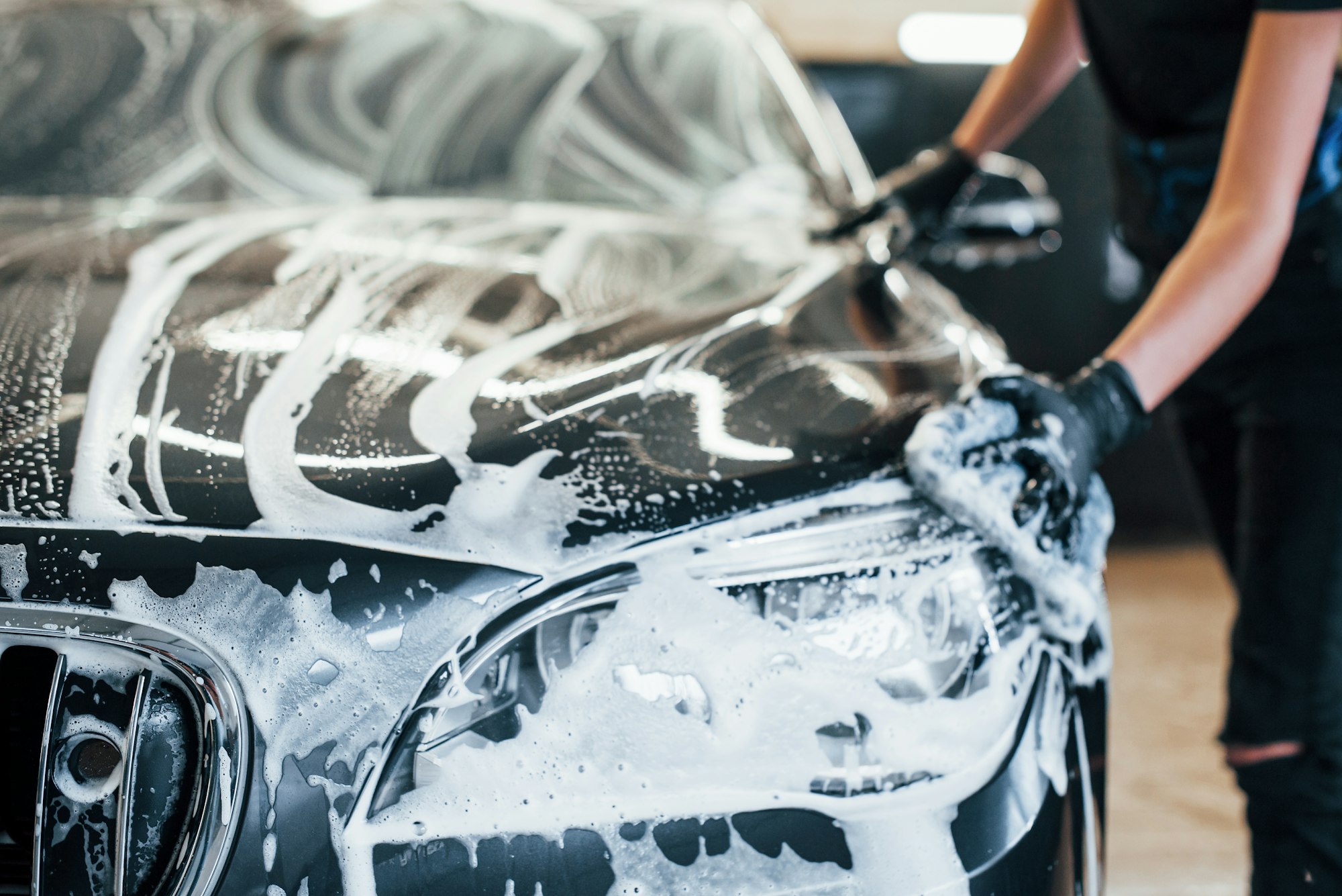 Modern black automobile get cleaned by woman inside of car wash station